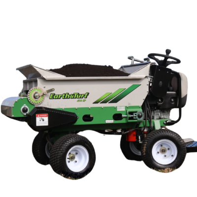 Ride-on turf aerator labeled 'Earth & Turf' with a dirt-filled hopper on top, parked on grass beside a tree.